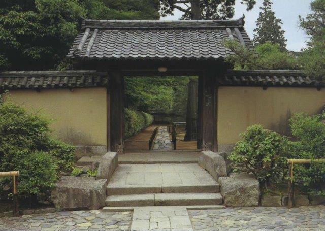 A stone bridge is seen in front of the roofed gate with its doors open.