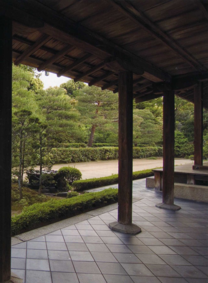 A sand-floored garden is seen through between the wooden pillars of the entrance hall.