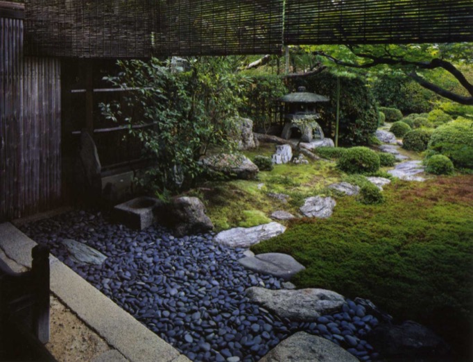 Small pebbles in dark blue grey are packed on the near side of the garden while a winding sequence of larger flat-top stones leads the way to a garden on the far side.