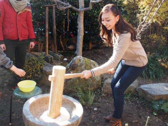 A Japanese lady is holding a wooden pestle of her arm's length that just landed on mochi in a mortal.