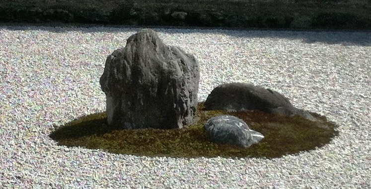 A squarish rock stands on the middle left, a smaller rock lies on the back right, an even smaller rock sits on the front right, all on a patch of moss.
