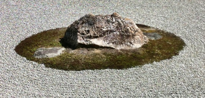 A medium-sized rock sits in the center of a moss patch, flanked by a pair of flat-top rocks embedded in the moss.